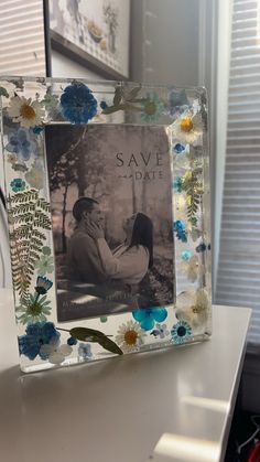 a photo frame with flowers on it sitting on top of a table next to a window