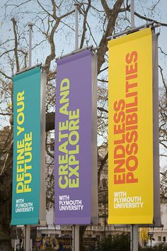 three colorful banners are hanging from the side of a pole in front of a tree