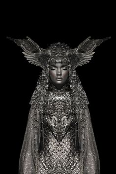 a statue with wings on it's head and dress in front of a black background