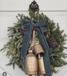 a wreath with two bells hanging from it's side and pine cones on top