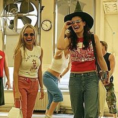 two women are laughing and talking on their cell phones in a room with other people