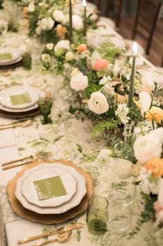 a long table is set with white and green flowers, gold place settings and candles