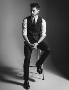 a man sitting on top of a chair wearing a suit and tie with his hands in his pockets