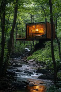 a small cabin in the woods with a river running through it and trees surrounding it