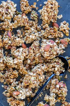 homemade granola with nuts and seeds on a blue surface next to a spoon,