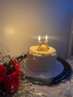 a white cake with two candles on top of it and flowers in front of it