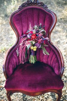 a purple velvet chair with flowers on the back and seat is sitting in some dried grass