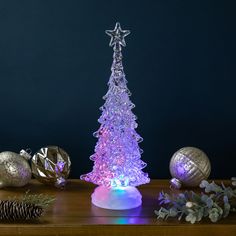 a lighted christmas tree sitting on top of a wooden table next to silver balls and pine cones