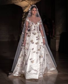 a woman in a white wedding dress with a veil on her head is walking down the runway