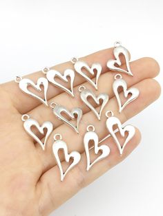 small silver heart charms in the shape of hearts on a person's hand with white background