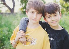 two young boys standing next to each other in the grass with trees in the background