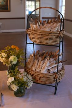 two baskets with forks and spoons are sitting on a table next to some flowers