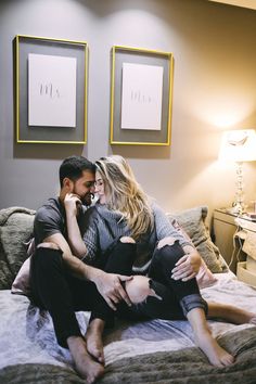 a man and woman sitting on top of a bed next to each other in a bedroom