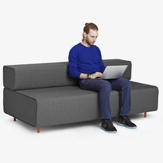 a man sitting on top of a gray couch using a laptop next to a blue ottoman