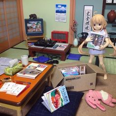 there is a doll holding a magazine in a room with other toys and books on the floor