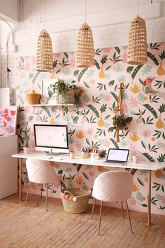 a desk with two computers on it in front of a floral wallpaper