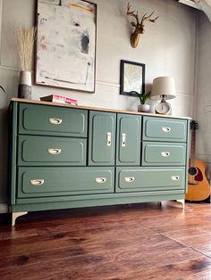 an old dresser is painted green and has deer heads on the wall next to it