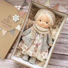 a small doll in a box next to a card and some paper garlands on a wooden table