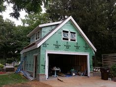 a green garage with the door open on a house being built in front of some trees