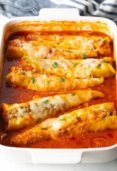 an enchilada dish with meat and sauce in it on a white table