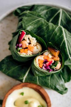 two wraps filled with vegetables sitting on top of a plate next to a bowl of dip