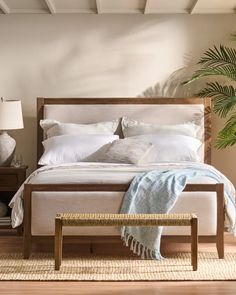 a bed with white linens and pillows in a bedroom next to a plant on the floor