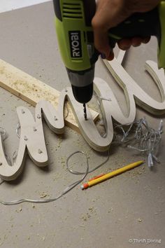 a person using a power drill to cut letters out of wood with nails and wire