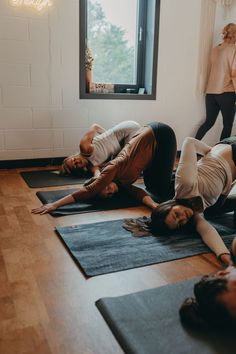 three people are doing yoga on mats in a room with large windows and wooden floors