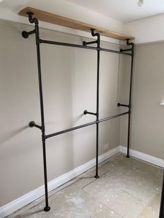 an empty room with some metal pipes on the wall and a wooden shelf above it