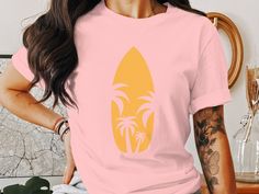 Embrace the summer vibes with this retro surfboard and palm trees graphic tee. Perfect for beach vacations, surfing adventures, or casual coastal living. This unique design brings a vintage beachy feel to your wardrobe. Ideal for both men and women who love seaside getaways and the sun-soaked surf culture. Available in short sleeve, long sleeve, and v-neck styles, this surf shirt is a must-have for your surf-inspired apparel collection.  Long Sleeve T-Shirt (Gilden 5400)  Fabrication: Fabric wei Tropical Printed Tops For Surfing, Tropical Printed Tops For Resortwear, Hawaiian Surfing Tops For Summer, Hawaiian Style Surfing Tops For Summer, Hawaiian Summer Surfing Tops, Hawaiian T-shirt For Surfing In Summer, Tropical Style Surfing T-shirt For Vacation, Tropical Surfing T-shirt For Vacation, Pink Relaxed Fit T-shirt For Surfing