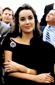 a woman with her arms crossed in front of a group of people wearing suits and ties