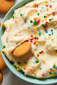 a bowl filled with frosting and sprinkles next to cookies