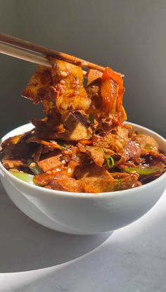 a bowl filled with meat and vegetables on top of a white table next to a wooden spoon