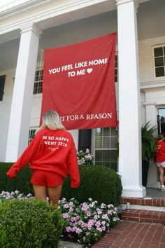 two women in red shirts are walking towards a house with a sign that says you feel like home to me