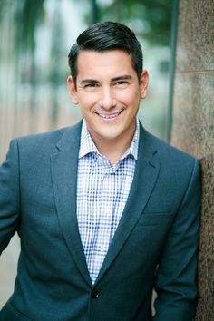 a man in a suit leaning against a wall smiling at the camera with his hands on his hips