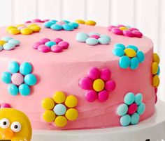 a pink cake decorated with flowers and a yellow chick on the side, sitting on a white pedestal