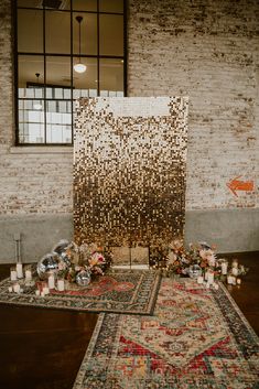 an area with rugs, candles and flowers on the floor in front of a brick wall