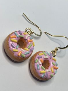 two donuts with sprinkles on them are hanging from gold ear wires