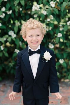 a young boy in a tuxedo smiles at the camera