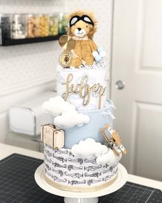 a teddy bear sitting on top of a blue and white tiered cake with clouds