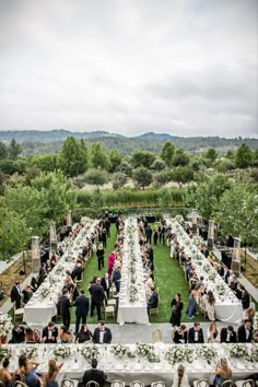 an outdoor wedding reception with long tables and white linens, surrounded by greenery