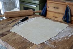 a wooden cutting board topped with dough next to a knife and rolling pin on top of it