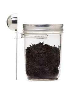 a glass jar filled with black tea next to a metal scooper and ladle