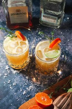 two glasses filled with orange and lime margaritas on top of a wooden cutting board