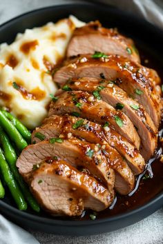 sliced pork, mashed potatoes and green beans in a black bowl with gravy