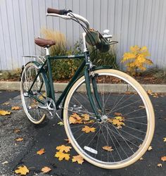 a green bicycle parked in front of a building with yellow leaves on the ground next to it