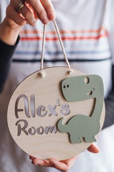 a person holding a sign that says alex's room with a dinosaur on it