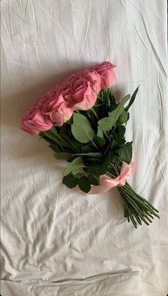 three pink roses sitting on top of a white sheet with green leaves and stems in between them