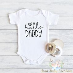 a white baby bodysuit with the words hello daddy on it next to a pacifier