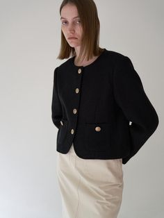 This is a tweed jacket with a round neckline, offering a modern twist on classic outerwear. It's designed with a button-down front, featuring prominent buttons that stand out against the fabric. The jacket has two patch pockets at the front, providing both function and a decorative element. The material gives the impression of a knit texture, which suggests that it's intended for warmth and comfort.- The round neckline provides a soft, feminine touch and allows for various underlayering options.- The buttons add a contrasting detail that enhances the jacket's visual appeal.- The jacket's cropped length makes it an ideal piece for pairing with high-waisted bottoms or over dresses. Classic Black Tweed Jacket With Button Closure, Winter Workwear Tweed Jacket With Buttons, Classic Black Tweed Jacket With Buttons, Winter Office Tweed Jacket With Button Cuffs, Fall Tweed Jacket With Buttoned Pockets For Work, Classic Wool Blazer With Buttoned Pockets, Tweed Jacket With Buttoned Pockets For Work, Tweed Outerwear With Buttoned Pockets For Fall, Winter Tweed Blazer With Buttoned Pockets